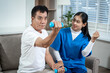 © Thitaporn - An older man exercises with a dumbbell while a caregiver or nurse supports him during home rehabilitation on a sofa