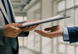 © MdMusiur - Business person handing a clipboard with papers to a colleague in the office