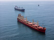 © Amazing Aerial - Aerial view of two large cargo ships sailing in the open ocean, with a red bulk carrier in the foreground and a dark blue vessel in the distance near Cascais, Lisboa, Portugal.