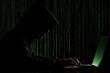 © Mochi - Silhouette of person in hooded sweatshirt typing on laptop, green digital matrix background