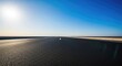 © Sathaporn Buarabut - An empty asphalt road stretches toward the distant horizon under a clear bright sky, creating a minimalist and expansive landscape image, blue, freedom, endless