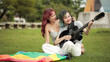 © vittaya - Asian Woman Hugging Girlfriend Playing Acoustic Guitar in Park with Rainbow Flag