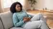 © Marina P. - Woman holding abdomen in pain on sofa at home