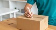 © Tsubasa - Person writing on a cardboard shipping box with a stylus pen, preparing for delivery, close-up shot