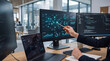 © Asiya - Analyst pointing at digital network graph on monitor with data charts during office work with blurred background