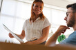 © Studio Marmellata - A female employee smiles while presenting a document to her male colleague during a meeting in a bright office. They are collaborating on a new work project together.