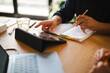 © Studio Marmellata - A professional collaborates on a project at a desk. He points at a digital tablet while holding a pencil and taking notes in an open notebook to organize his work.