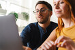 © Studio Marmellata - A focused man with glasses and a woman collaborate on a professional task while looking at a laptop screen together in a bright and modern open workspace environment.