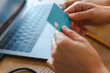 © Studio Marmellata - A person holds a bank card in their hands while sitting in front of an open laptop. They are making an online purchase or managing their finances from home today.