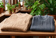 © Pixel-Shot - Sustainable fashion and cozy winter wear, two folded ribbed knit sweaters on a wooden table with green plants