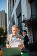 © Davor - Senior businessman reviewing documents on laptop at outdoor city cafe