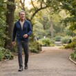 © Edina - A man in casual attire walks through a park on a paved path, enjoying a peaceful stroll amidst lush greenery and dappled sunlight.