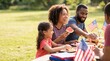 © SimpleDesignStudio - Happy African American family enjoying a picnic celebration with flags and food outdoors
