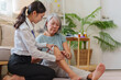 © Natee Meepian - Young Asian female doctor examining senior patient knee at home