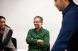 © Johnér - Smiling mature businessman sitting with arms crossed while interacting with colleagues in meeting
