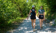 © JairoMZ - Two women walking together on a gravel forest trail during a hike, carrying backpacks and wearing outdoor clothing while moving through a wooded landscape and generous copy space