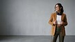 © NimVisuals - Trendy young woman posing in a stylish suede blazer and dark trousers against a minimalist grey background.