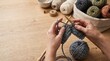 © Hina - Hands holding wooden knitting needles with grey wool on a rustic table