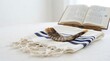 © Mona - A shofar horn resting on a tallit prayer shawl with an open prayer book in the background, symbolizing jewish religious traditions and holidays