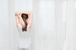 © CaoYen - Young woman stretching by window at home in morning routine