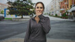 © Krakenimages.com - Woman covering mouth with hand on street while looking surprised, wearing dark gray zip pullover and bun hairstyle; surprise concern.