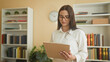 © Krakenimages.com - Young woman holds clipboard and points pen while reading notes in an office building with bookshelves and clock; focused evaluation.