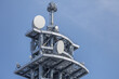 © thomasgweber - Multi-level matte gray telecommunications tower with lattice framework supporting radome covered parabolic dishes and vertical antennas set against a clear blue sky.