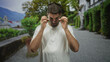 © Krakenimages.com - Man with beard and glasses adjusts eyeglasses with both hands while looking down on a gravel walkway beside a building entrance; quiet contemplation.
