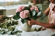 © NICONICO - Florist arranging pink hydrangea and eucalyptus bouquet in vase on marble table