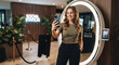 © Максим Новосветлов - Smiling young woman taking a selfie with smartphone in modern office lounge interior with social booth setup.