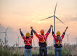 © BESTIMAGE - Workers teamwork discussing wind turbine power generator sustainability performance inspection together at Renewable Energy Plant Backside engineers raising hands success near windmill at sunset