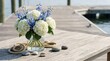 © Purepixels - A serene marina fest arrangements centerpiece featuring fresh blue delphiniums and white hydrangea flowers in a glass vase on a rustic weathered wood deck