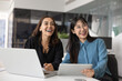 © fizkes - Two happy diverse women teammates, corporate employees take break seated at desk with tablet and laptop, distracted from workflow, looking away, laughing, enjoy positive, friendly talk with colleagues