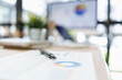 © David - Pen rests on a financial report displaying a pie chart and graphs, representing business analysis, strategic planning, and market research on a blurred office desk