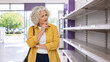 © Vyatcheslav - Concerned senior woman looking at empty shelves in a supermarket. Elderly female shopper worried about product shortages and supply chain issues