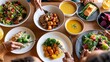 © The Little Hut - Overhead view of a diverse, healthy meal spread with various dishes and hands reaching for food