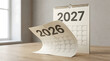 © Strabiliante - Turning calendar page from 2026 to 2027 on wooden desk