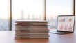 © twc - A tall stack of important business documents and paper reports sit on an office desk next to a modern laptop with financial chart graphs