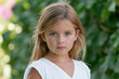 © Studio ANNA - Young girl's portrait capturing childhood innocence and natural beauty, standing in a sunny outdoor setting with green foliage