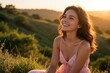 © Maryna - Smiling young caucasian woman in pink dress enjoys sunset in countryside. Happy girl sits on grassy hill during golden hour. Beautiful female feels freedom, peace in nature. Summer evening landscape