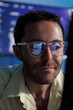 © SAT65 - Concentrated software developer coding at computer with programming interface reflected on glasses while reviewing source code and working on coding task sit at desk in tech office at night.