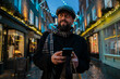 © Westend61 - A bearded man uses a smartphone while shopping on a festive street