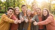 © julijadmi - Group of teenagers smiling and giving thumbs up in a sunlit park, wearing casual clothing and enjoying a cheerful moment outdoors