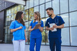 © Dragana Gordic - Smiling Medical Team of Nurses and Doctor Discussing Patient Care With Tablets Outside Hospital