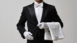 © Lemonkey - A professional butler in a tuxedo with white gloves and a cloth napkin standing against a grey background.