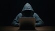 © PixelXpert - Mysterious hooded figure working on a laptop computer in a dark room representing digital cyber crime security