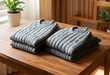 © Pixel-Shot - Cozy knitwear and sustainable fashion, two folded gray sweaters on a wooden table with natural light and a houseplant