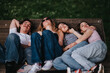 © qunica.com - Four friends lie closely together on a wooden park bench, resting with eyes closed. A group of school friends relax outdoors, sharing a quiet moment on a sunny day.