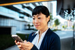 © Davor - Professional businesswoman using smartphone outside modern office