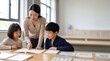 © ASMA - Teacher Helping Young Students Study Together in Classroom with Books and Creative Learning Activities